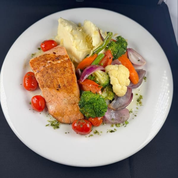Grilled salmon fillet with mashed potatoes, roasted cherry tomatoes, broccoli, cauliflower, carrots, and red onions.
