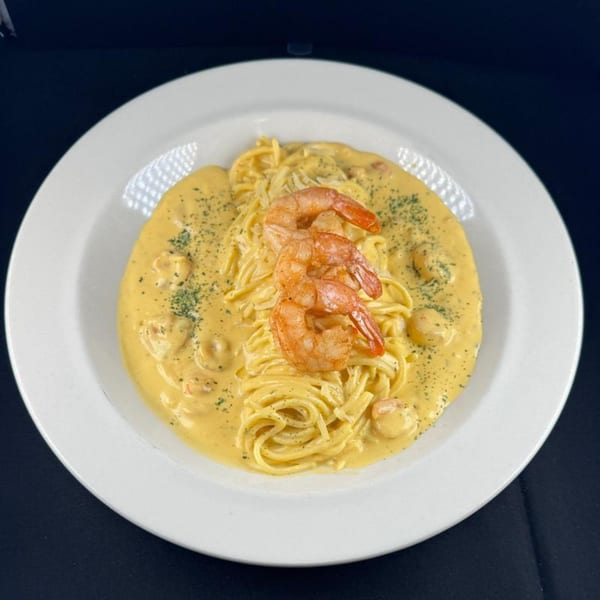 Spaghetti with creamy yellow sauce, topped with three large shrimp and sprinkled with herbs.