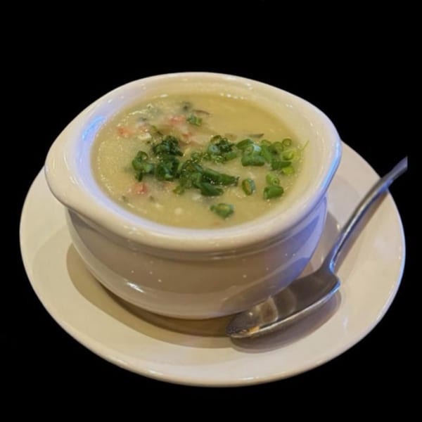 A bowl of congee with green onions and meat, served on a white plate with a spoon.