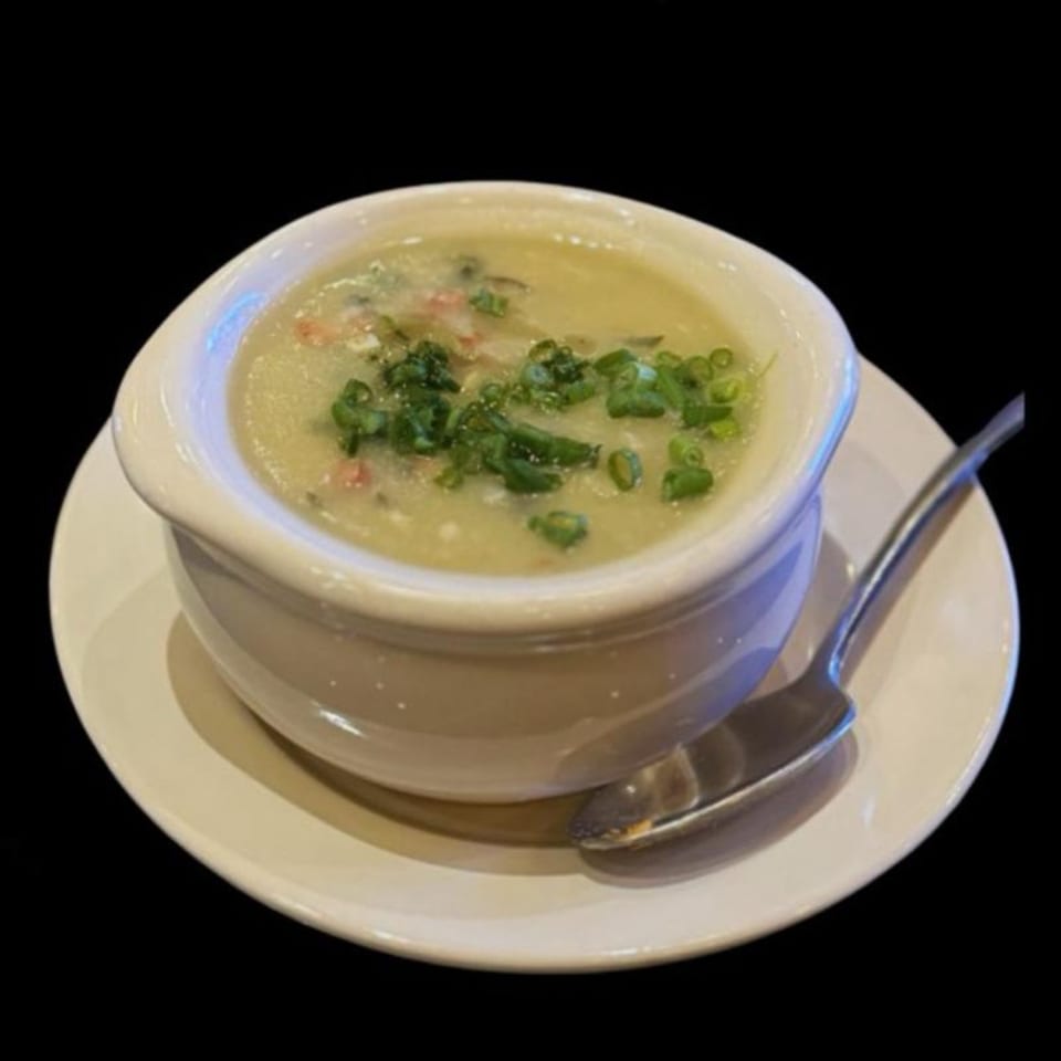 A bowl of congee with green onions and meat, served on a white plate with a spoon.