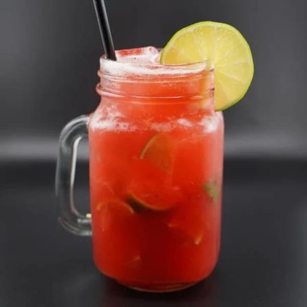 A vibrant red drink in a mason jar, garnished with a lime slice and a black straw.