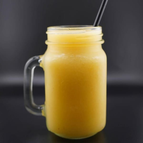 A vibrant yellow smoothie in a mason jar with a black straw against a dark background.