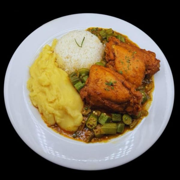 Fried chicken pieces with okra stew, white rice, and fufu on a white plate.