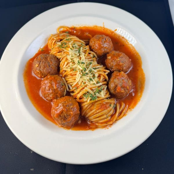 Spaghetti with meatballs and marinara sauce, topped with grated cheese and parsley on a white plate.