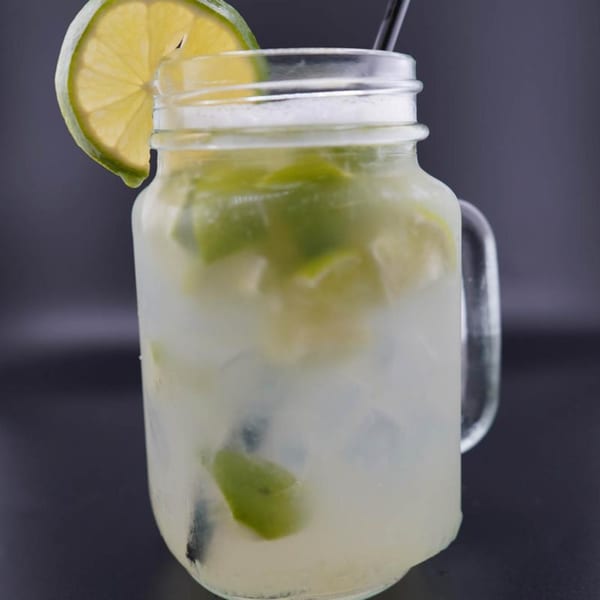 Refreshing lime drink in a mason jar with ice, lime slices, and a black straw.
