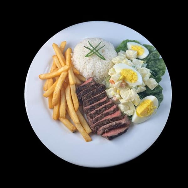 A white plate with sliced steak, french fries, rice, potato salad, and hard-boiled eggs.