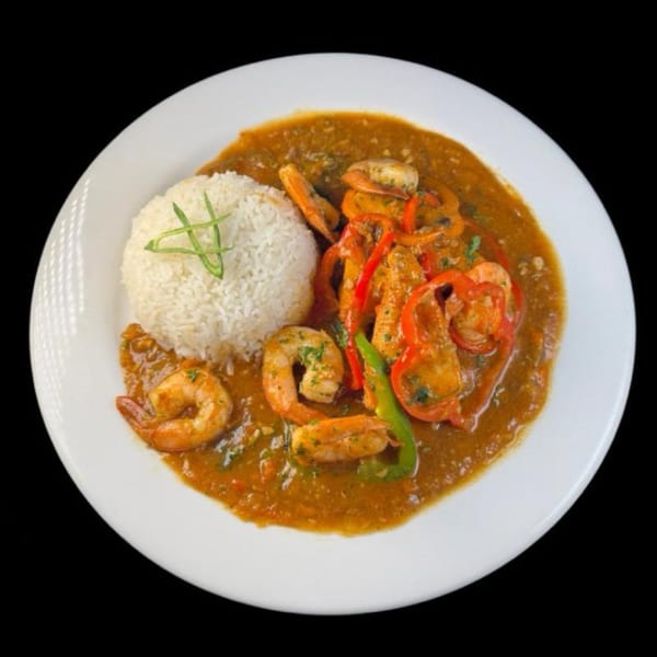 Shrimp creole with bell peppers and rice, garnished with green onions, on a white plate.